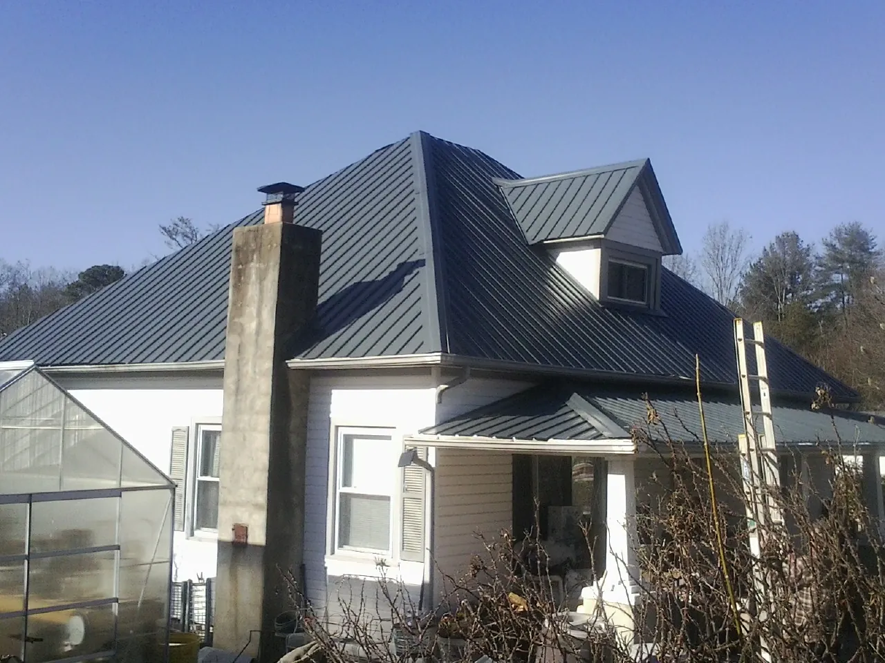 Dark blue standing seam metal roof on a white farmhouse with dormer — Slate & Tile Roof Repair by Roofing Brothers in Imlay City