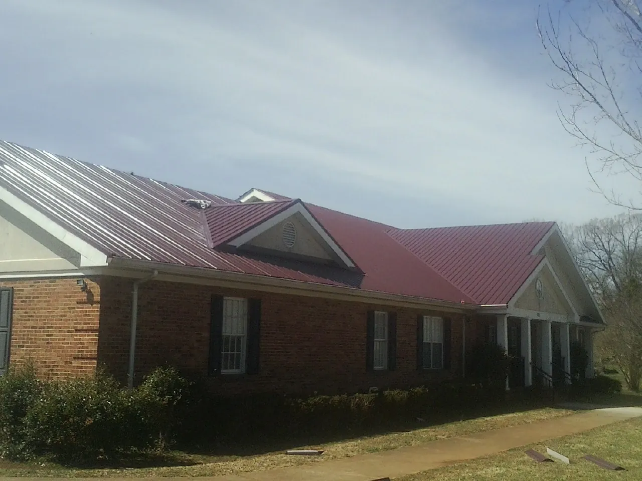 Red metal roof with gabled entries on a long brick building, from a Hail Damage Roof Repair job in Imlay City