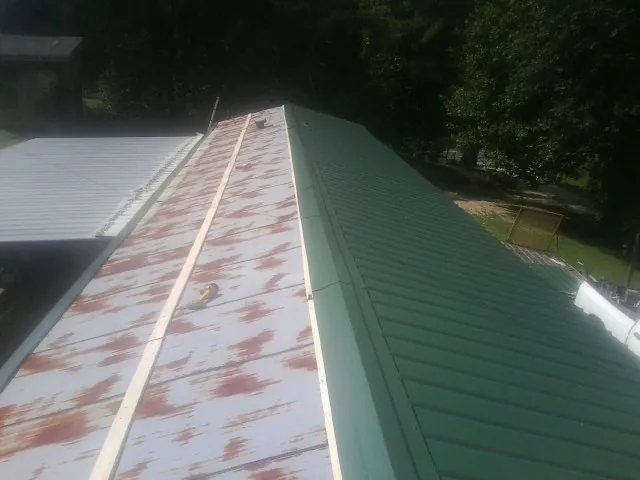 Old rusted panels beside newly installed green metal roofing — Wind Damage Roof Repair by Roofing Brothers in Imlay City