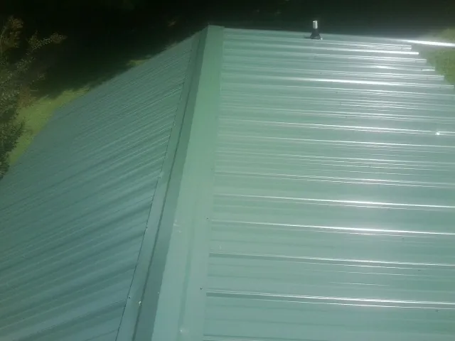 New green metal panels meeting at the ridge of a roof — Flat Roof Repair work by our crew in Imlay City