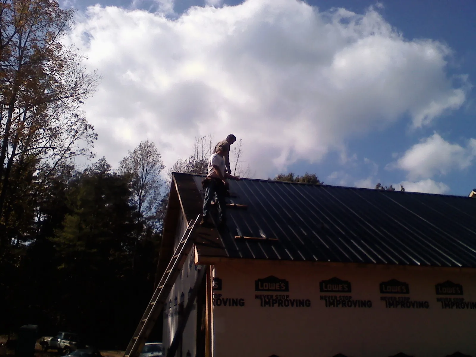 Roofer fastening dark metal panels high against a cloudy sky, from a Roof Inspection job in Imlay City