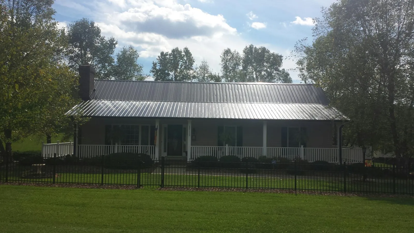 Gray metal roof on a brick ranch with a full width front porch — Gutter Guard Installation work by our crew in Imlay City