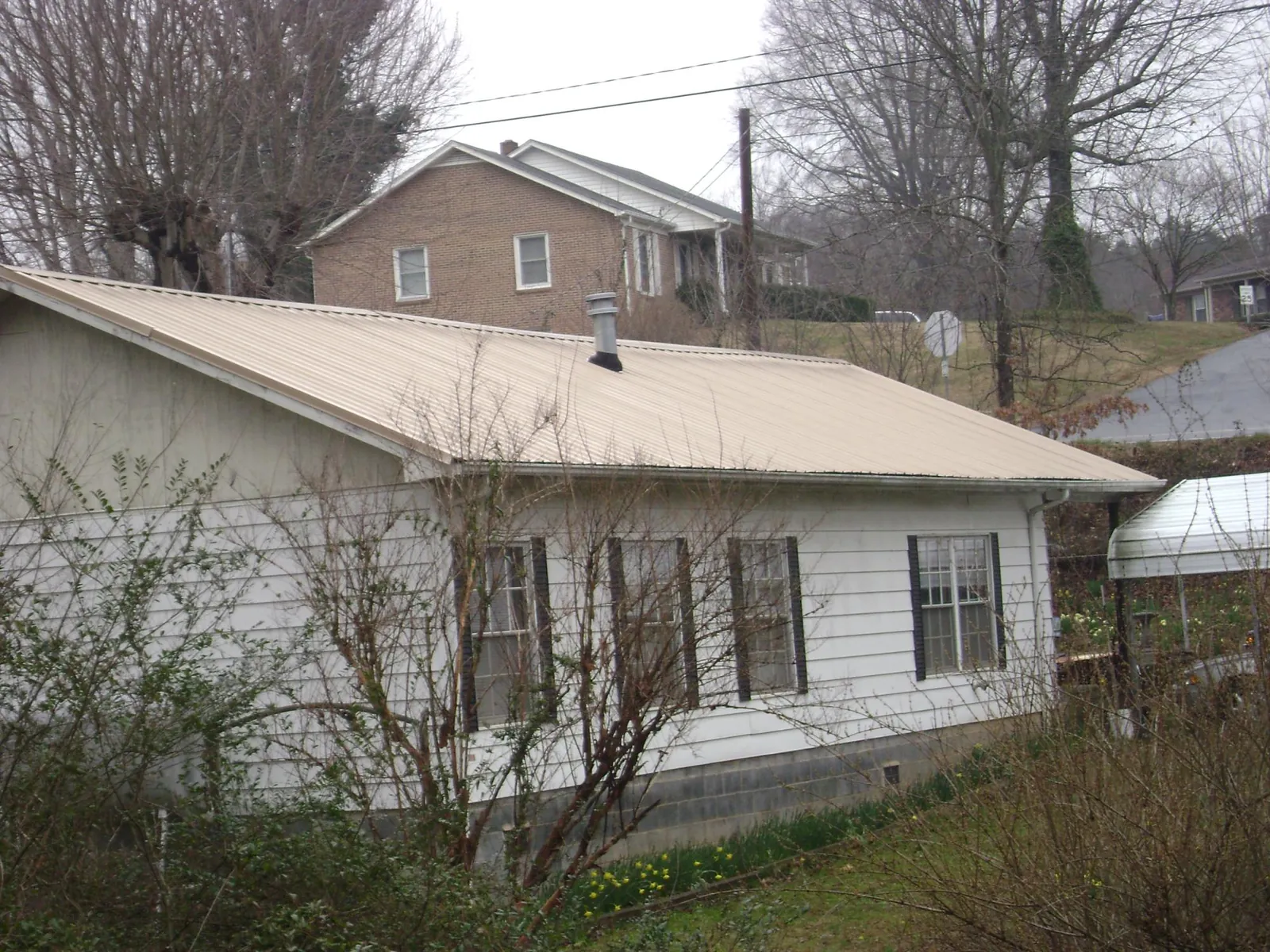 Tan metal roof on a white sided house set into a hillside — Commercial Roofing by Roofing Brothers in Imlay City