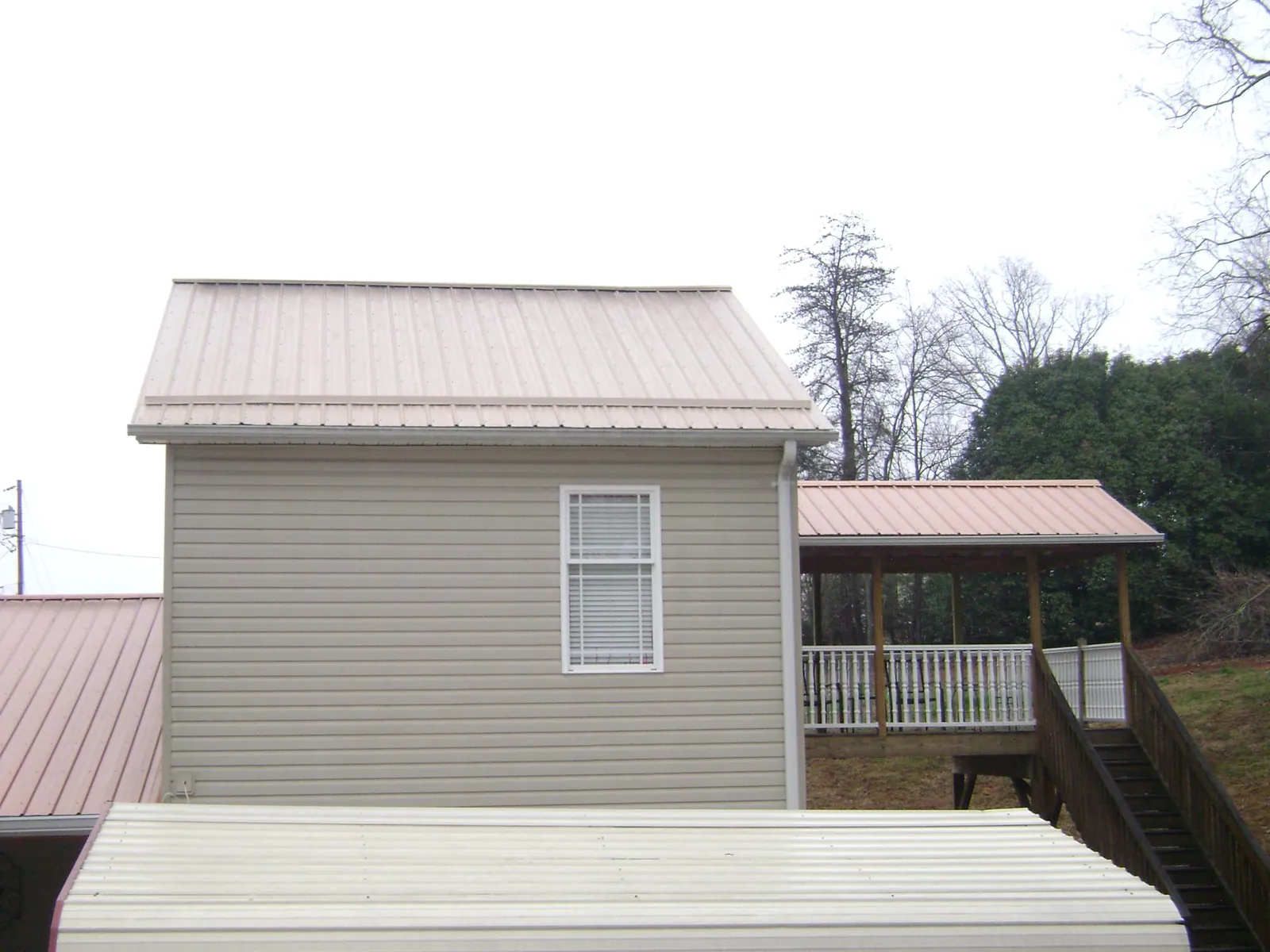 Tan metal roofs on a two story addition and attached porch, from a Roof Replacement job in Imlay City