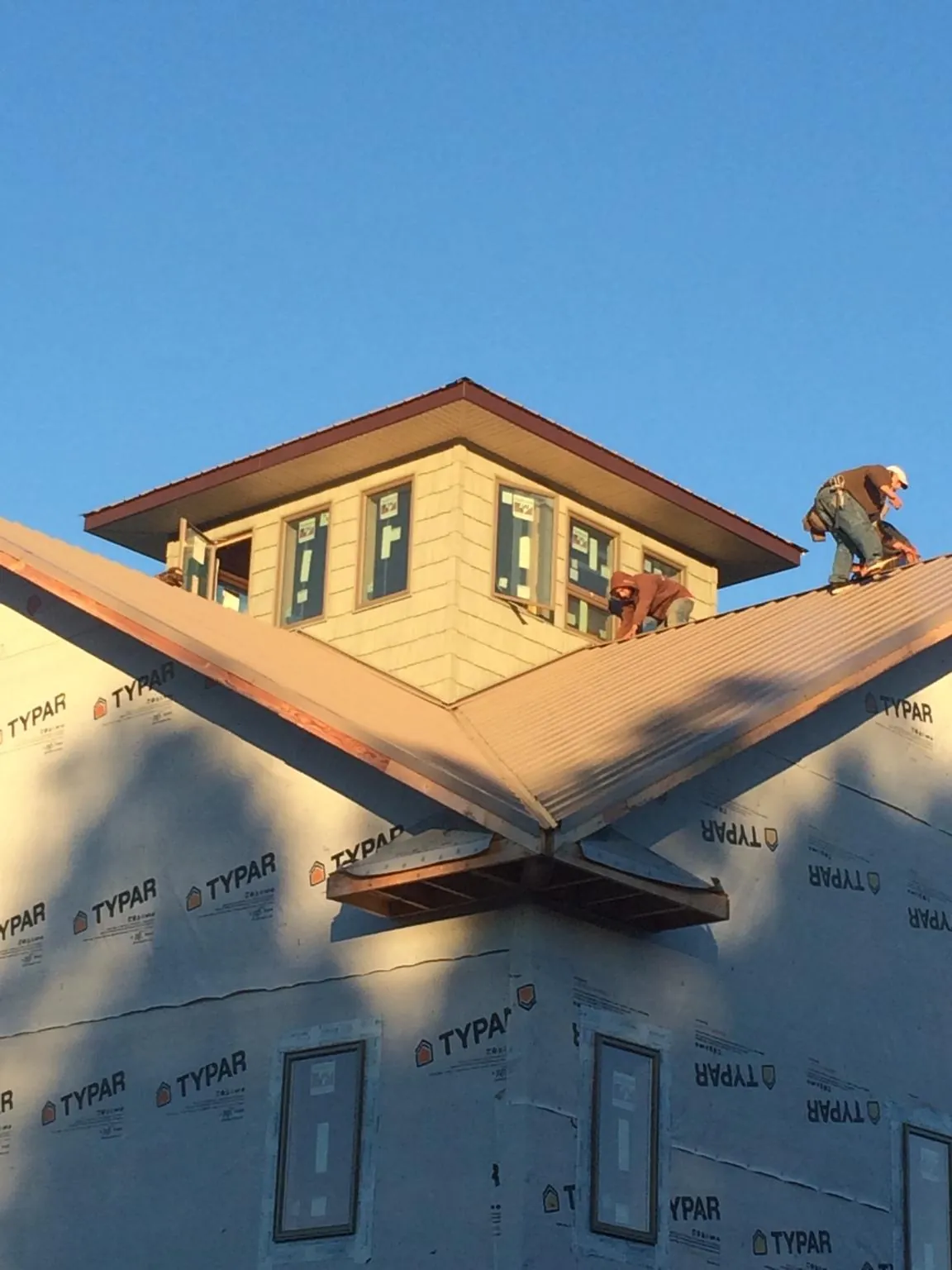 Roofers working around a rooftop cupola on a new metal roof at sunset — Roof Waterproofing in Imlay City by Roofing Brothers